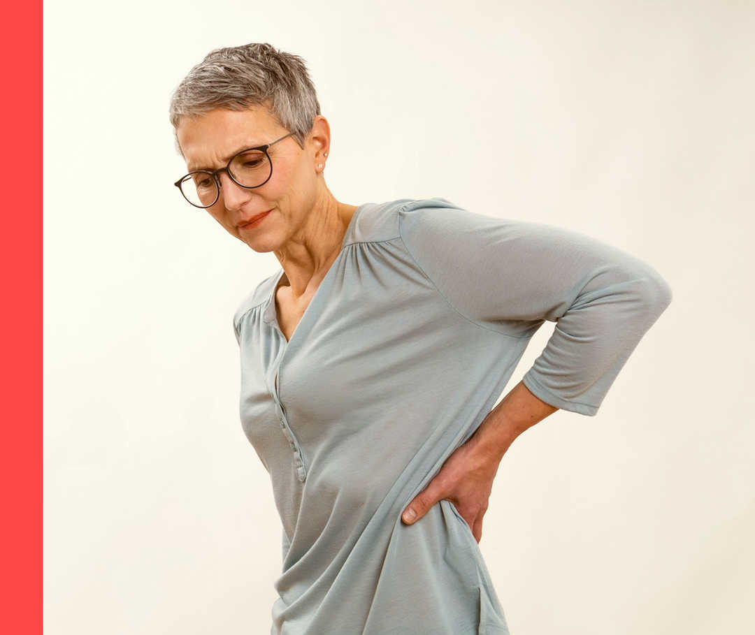 Eine Frau fasst sich an den Rücken und scheint Schmerzen zu haben. 