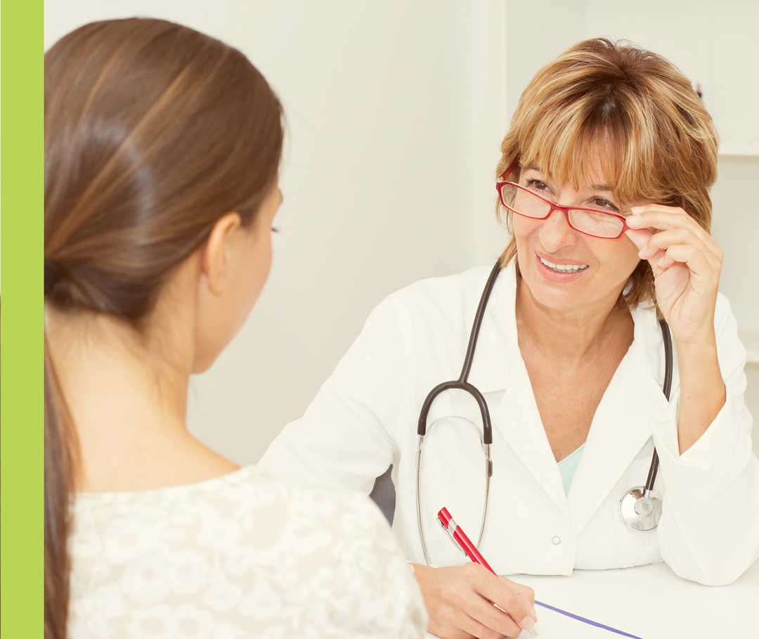 Eine Frau in weißem Kittel und mit umgehängtem Stethoskop unterhält sich mit einer anderen Frau.