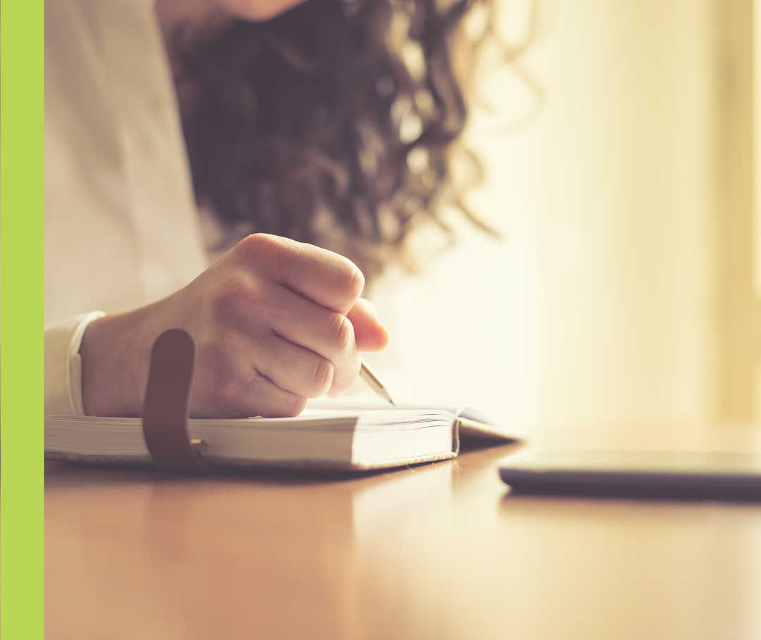 Eine Frau schreibt in ein kleines Buch.
