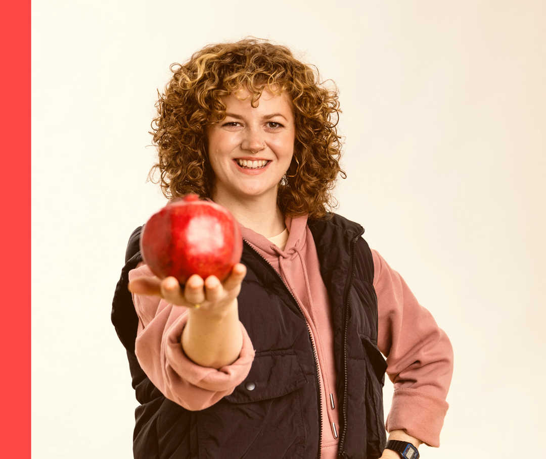 Eine Frau hält lächelnd einen Granatapfel in die Kamera.