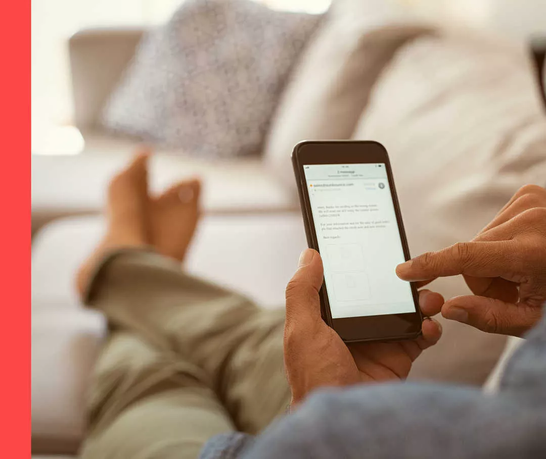 Bildausschnitt einer Person, die auf einem Sofa sitzt und ein Smartphone in der Hand hält.