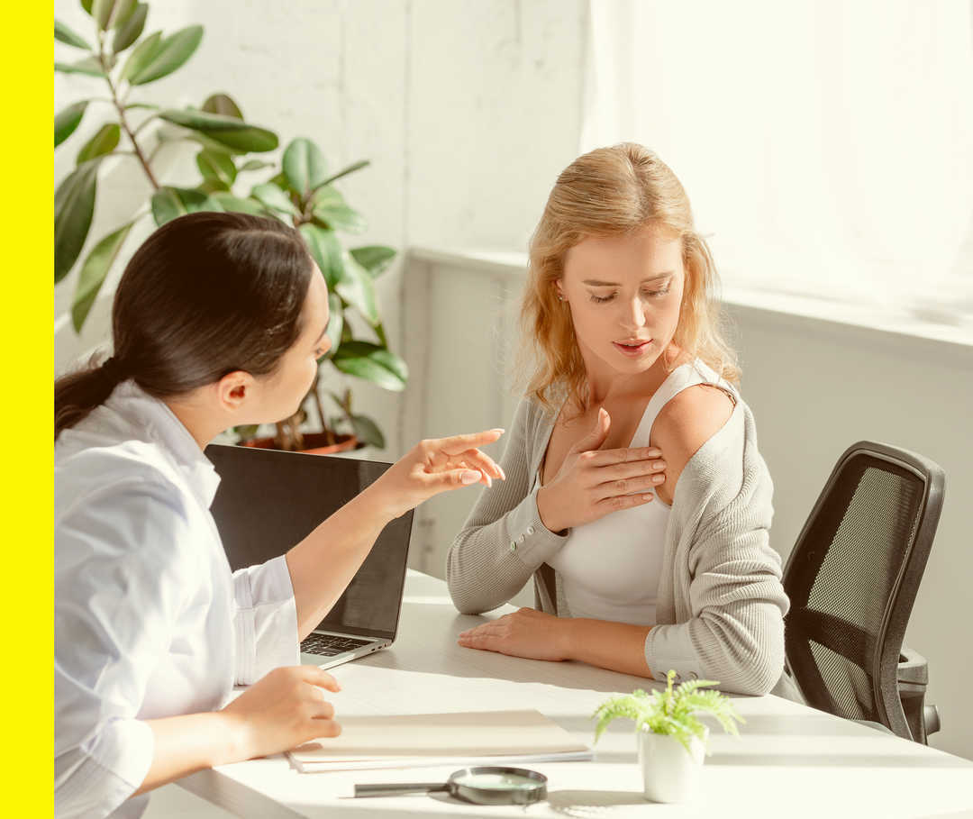 Eine Person im weißen Kittel begutachtet die entblößte Haut einer weiteren Person.