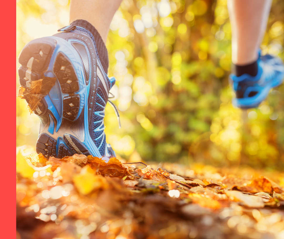 Nahaufnahme von Füßen in Sportschuhen, die im Freien über bunte Blätter laufen.