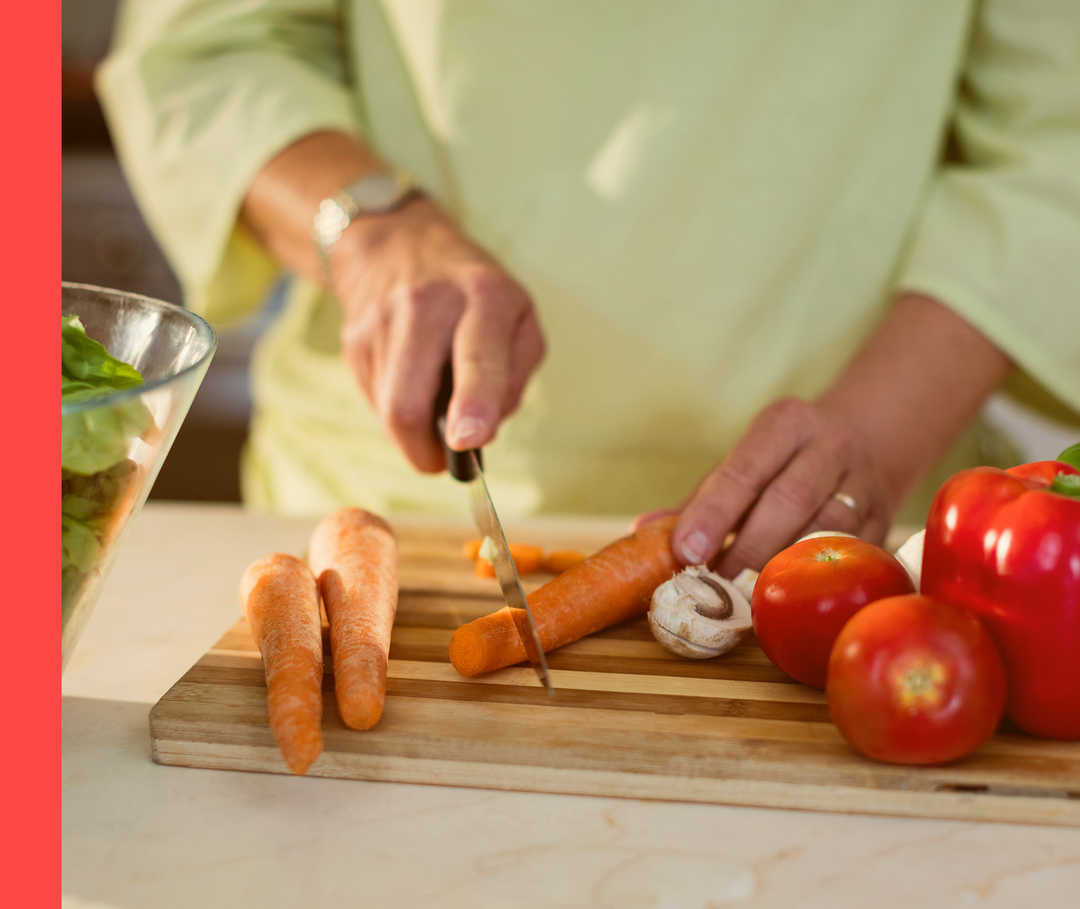 Nahaufnahme einer Person, die Karotten auf einem Holzbrett schneidet.