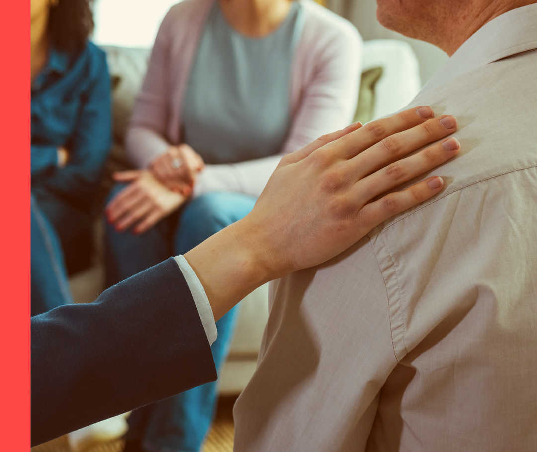 Nahaufnahme von mehreren Personen in einem Sitzkreis. Eine Person legt ihre Hand auf die Schulter einer anderen Person.