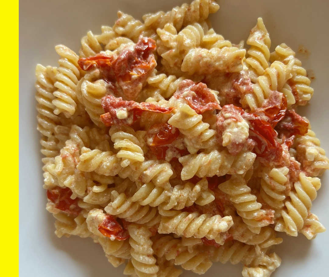 Ein Teller mit gekochten Nudeln, Tomaten und Feta.