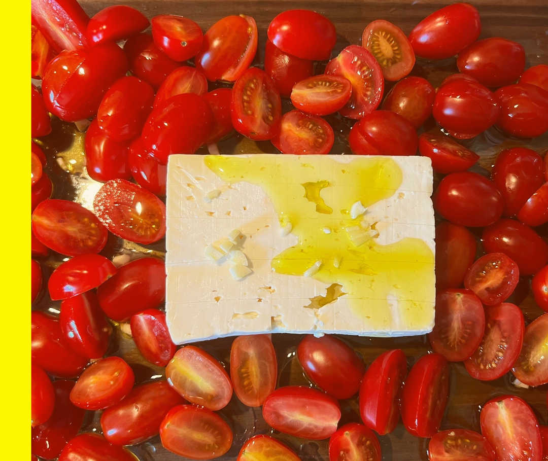Eine Auflaufform mit halbierten Cherrytomaten, Feta, Öl und geschnittenem Knoblauch.