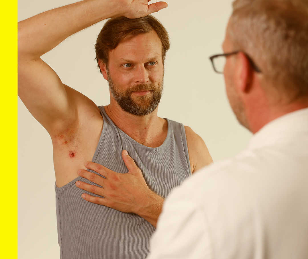 Ein Arzt und ein Patient unterhalten sich, der Patient hebt seinen Arm.