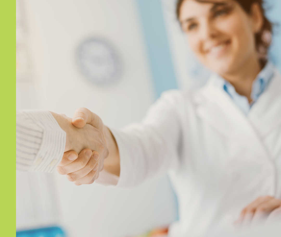 Eine lächelnde Person im weißen Kittel schüttelt einer anderen Person die Hand.