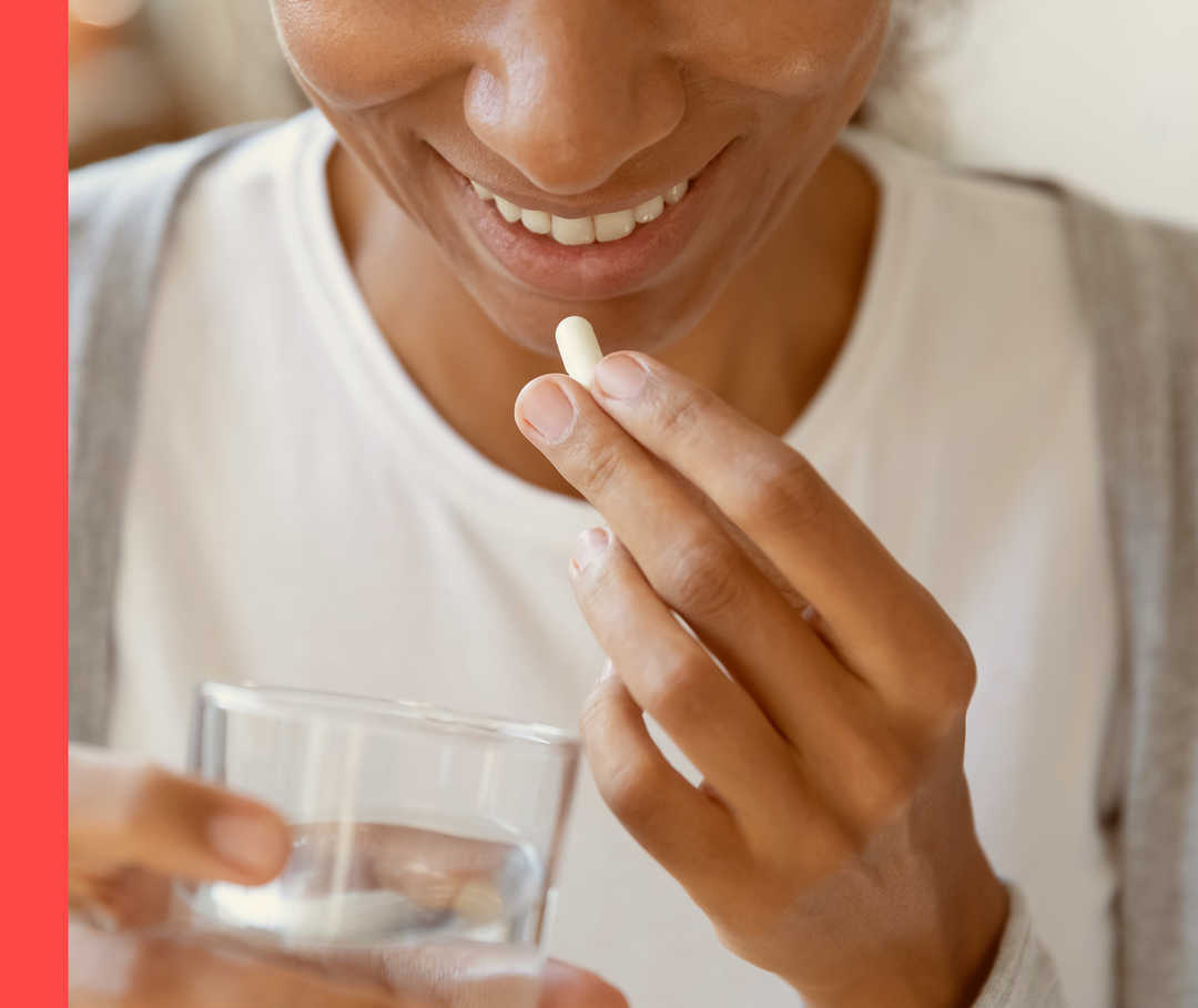 Eine lächelnde Frau hält eine weiße Pille und ein Glas Wasser in der Hand.