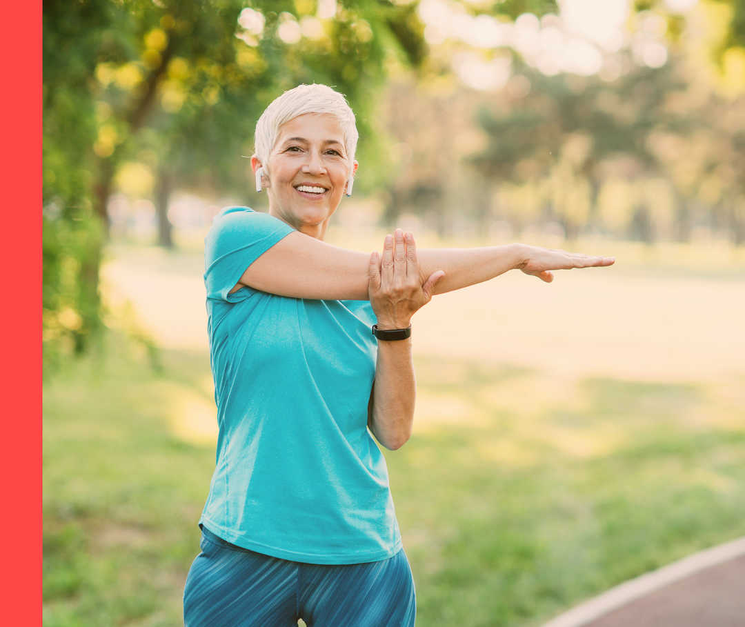 Eine lächelnde Frau in Sportkleidung dehnt ihren Arm.