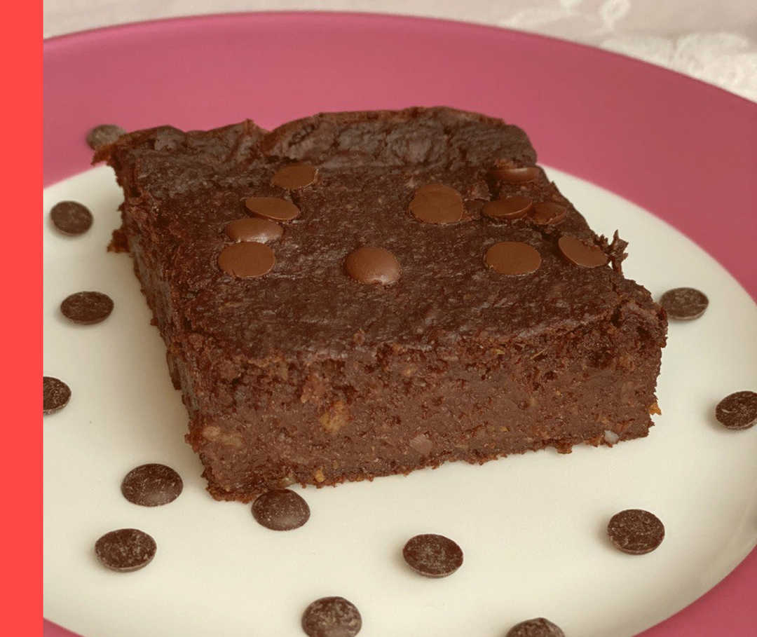 Nahaufnahme eines braunen Kuchenstücks auf einem Teller, der mit Schokoladenstückchen dekoriert ist.