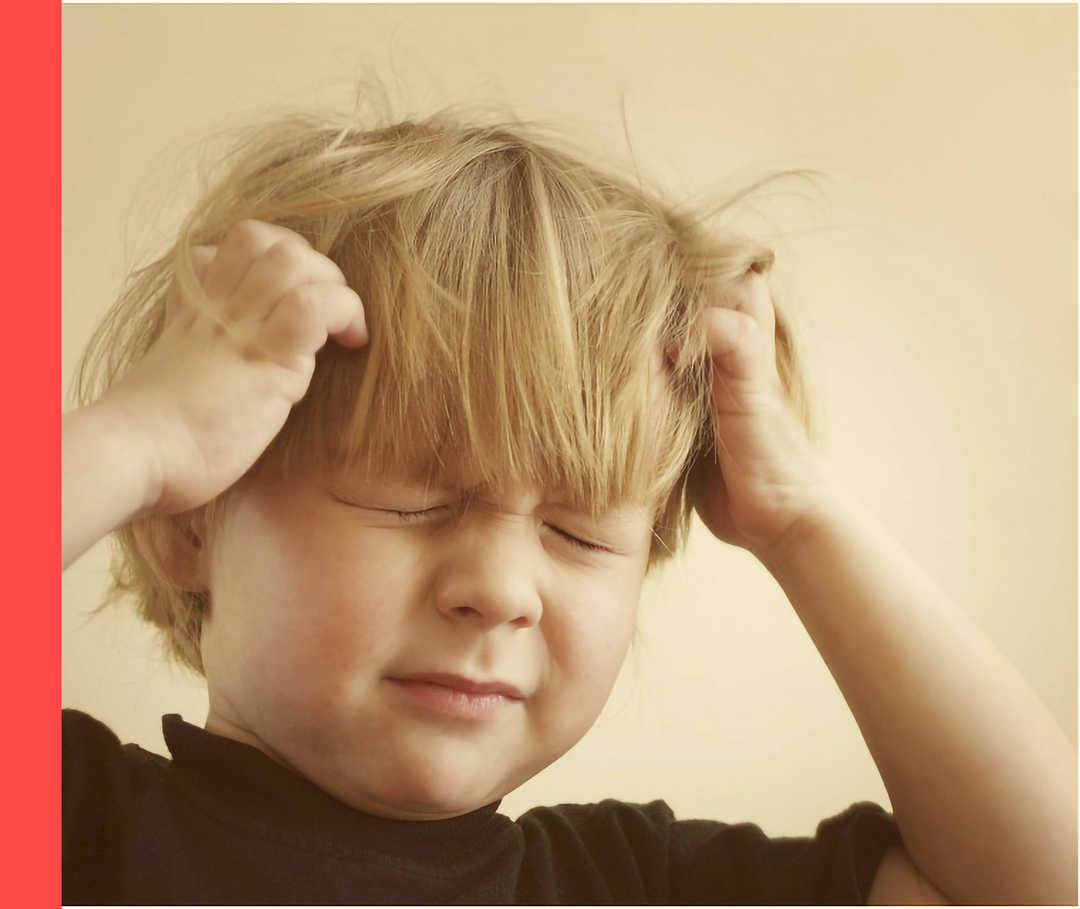 Ein kleiner Junge kratzt sich mit beiden Händen am Kopf.