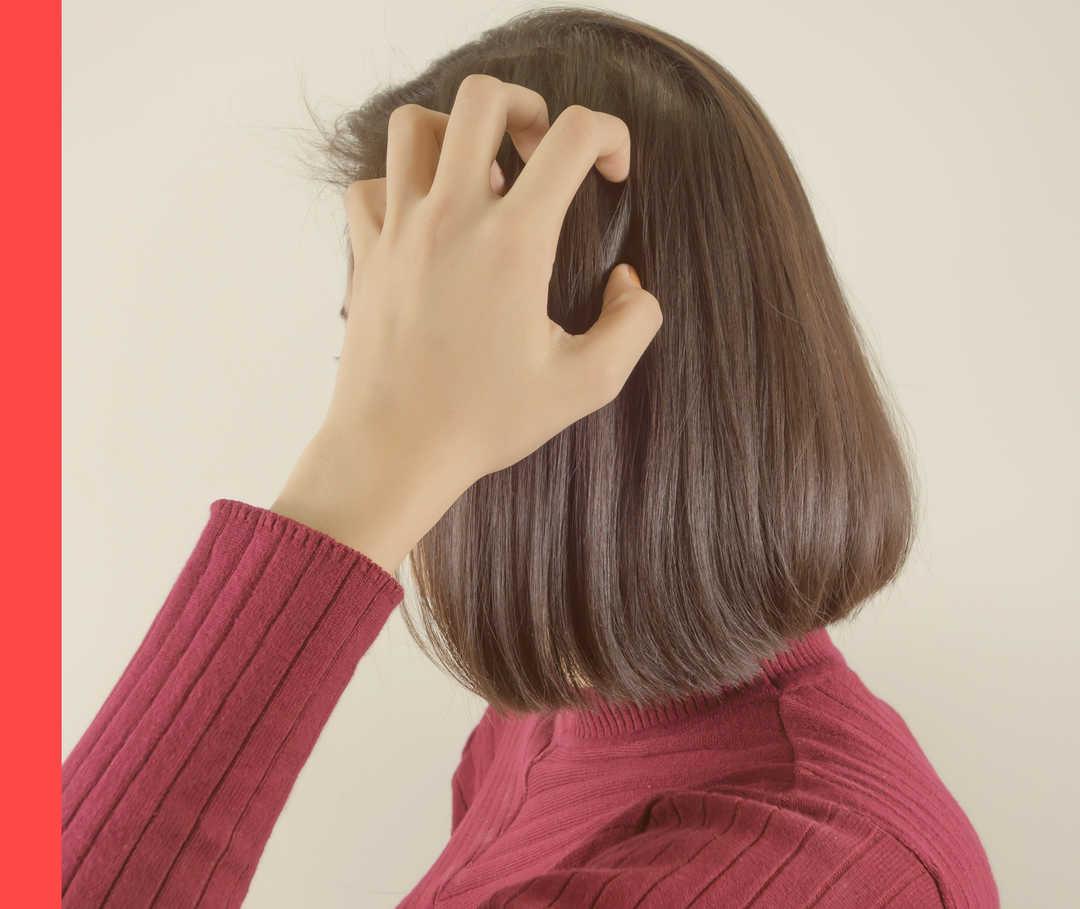 Eine Frau im weinroten Pullover von der Seite gesehen kratzt sich am Kopf.