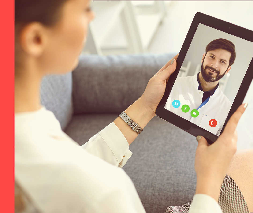 Person hält Tablet in der Hand. Auf dem Bildschirm ist ein Arzt zu sehen.