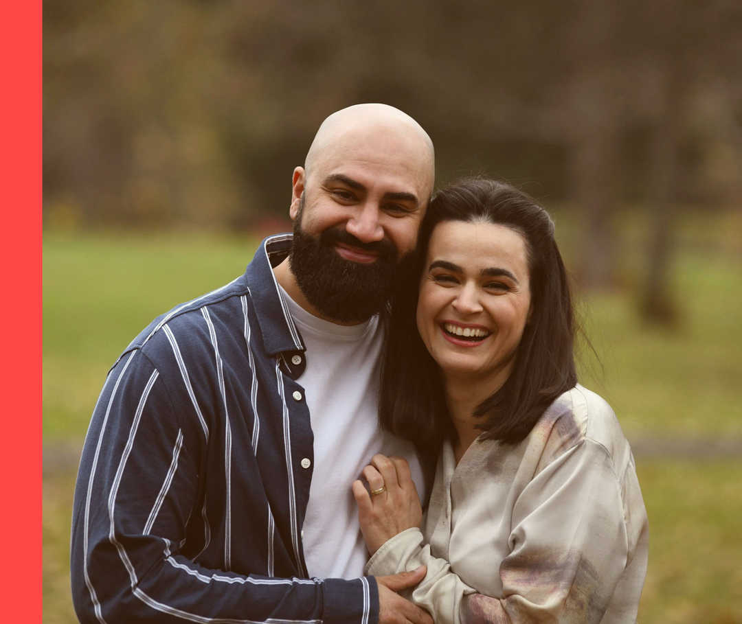 Sine und ihr Freund Umut stehen Arm in Arm im Freien und schauen lachend in die Kamera. 