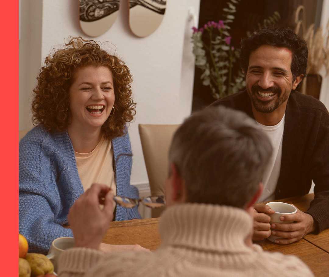 Drei Personen sitzen an einem Tisch und unterhalten sich lachend.