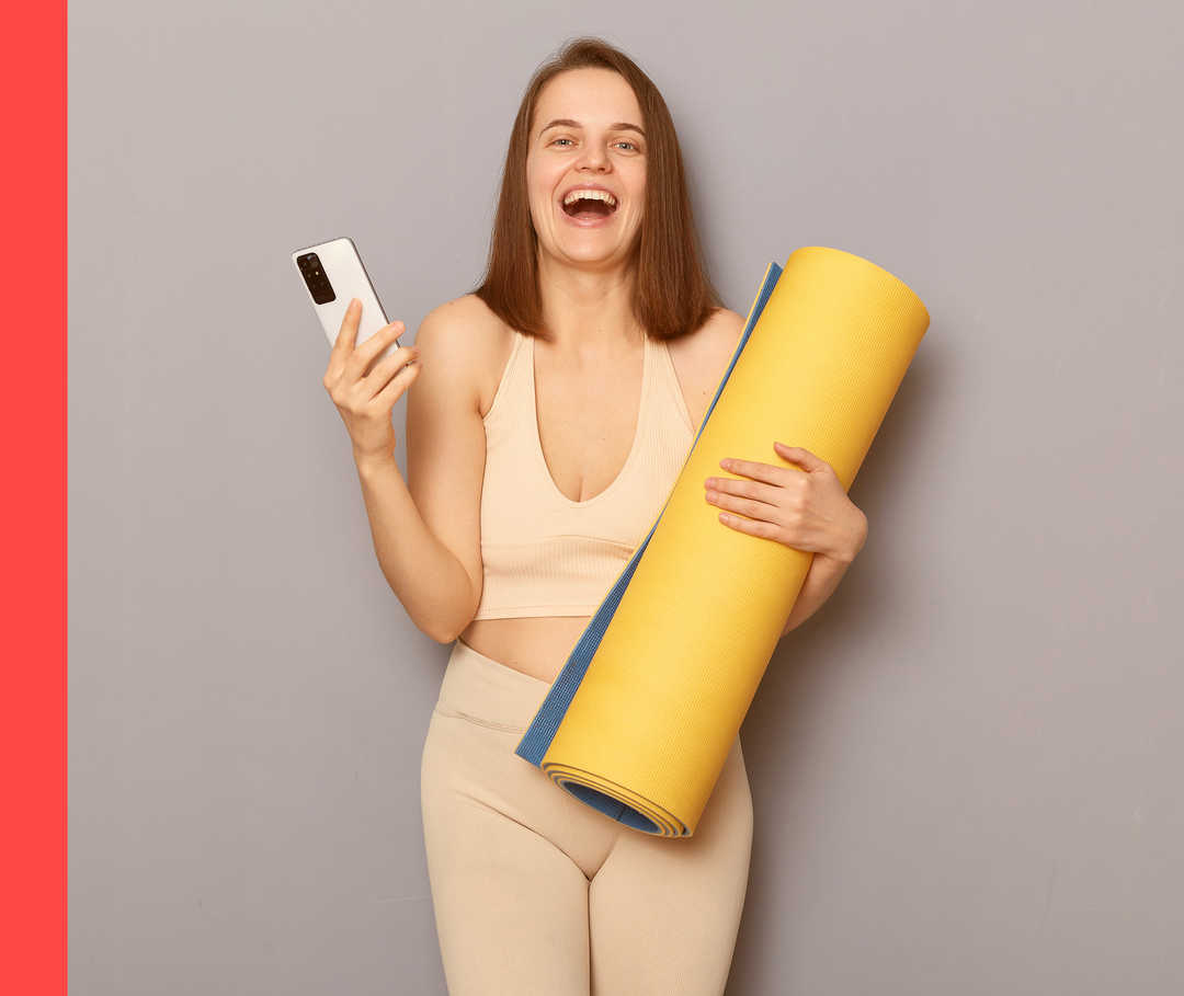 Eine Frau mit Yogamatte lacht in die Kamera.