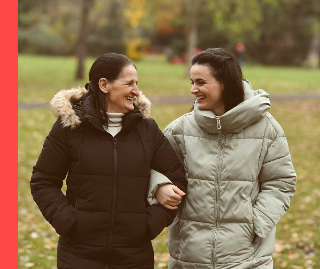 Sine hat sich bei ihrer Mutter eingehakt. Beide schauen sich lachend an. 