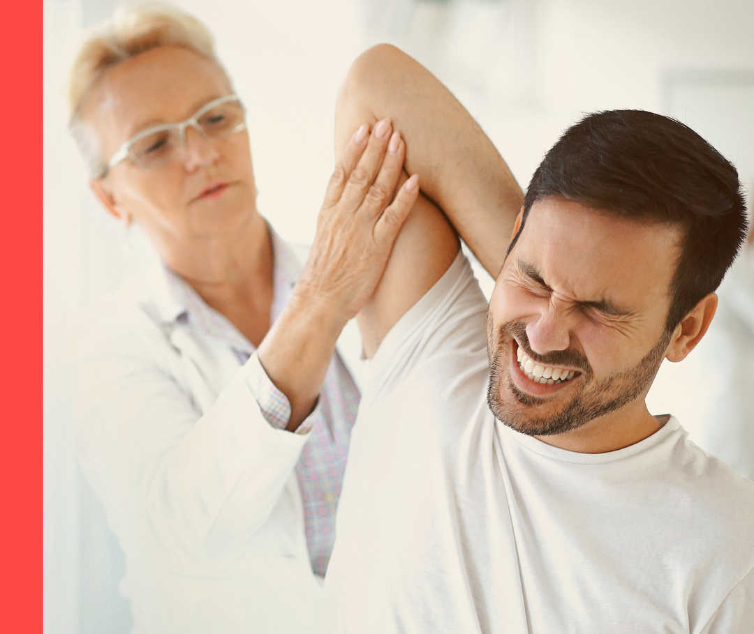 Mann im weißen T-Shirt fasst sich mit der rechten Hand und schmerzverzerrtem Gesicht an den Rücken. Hinter ihm steht eine Medizinerin, die seinen Arm berührt.