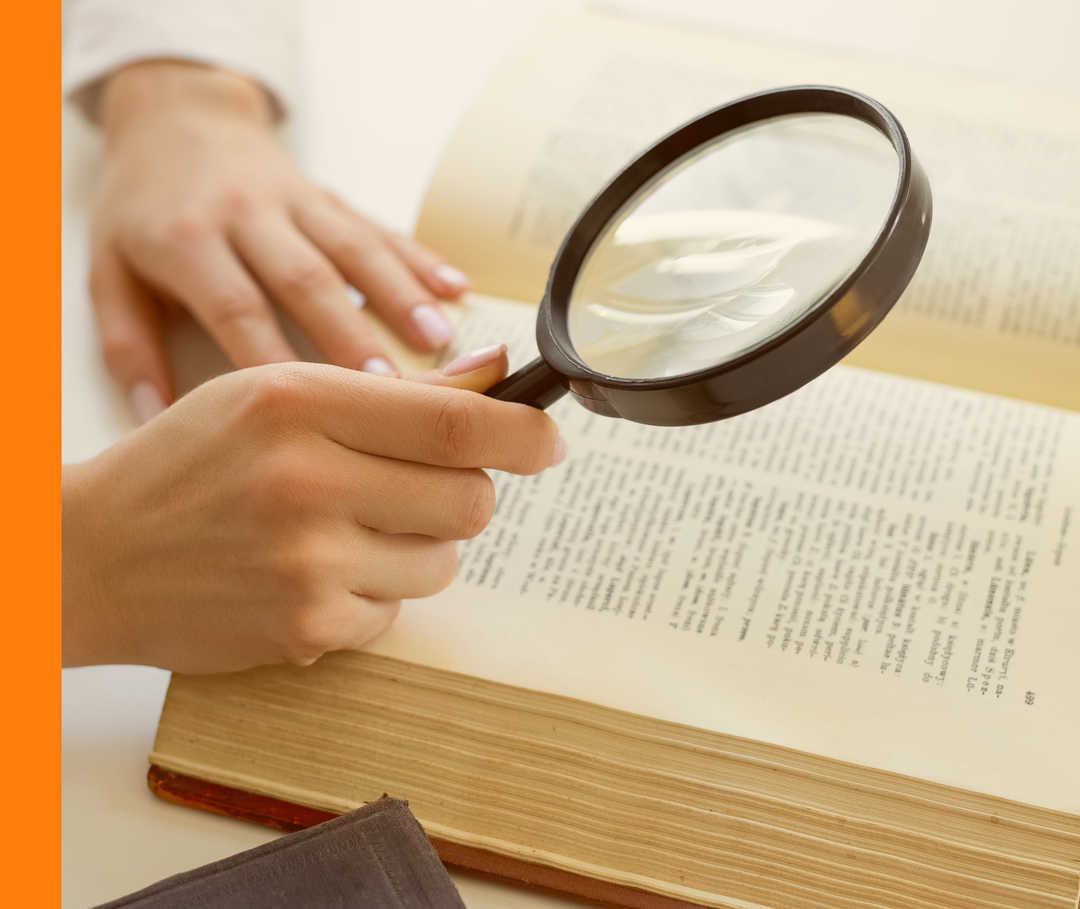 Eine Person hält eine Lupe über ein Buch.