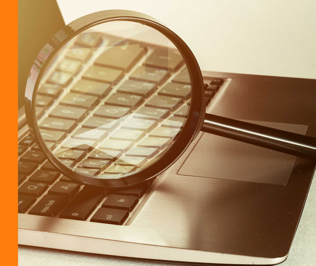 Eine Lupe liegt auf einem geöffneten Laptop.