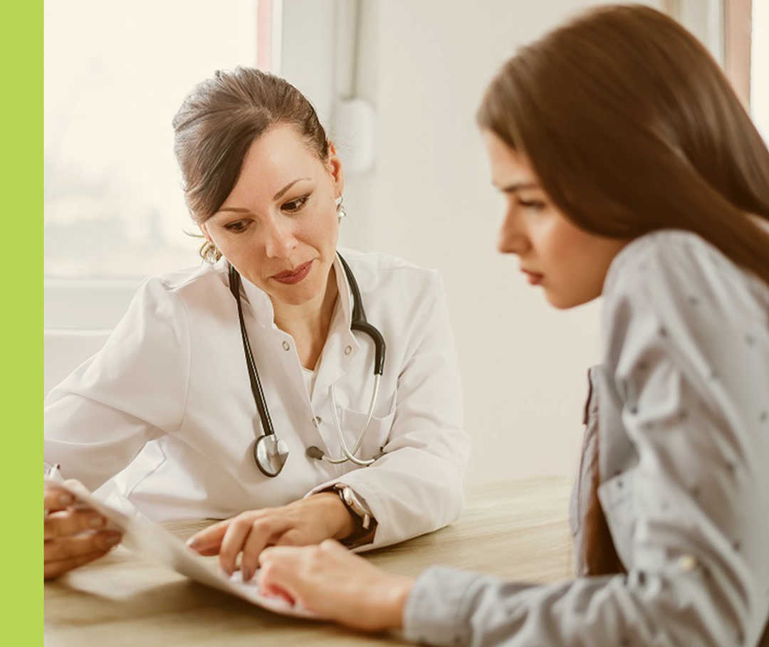 Eine Frau in einem weißen Kittel bespricht mit einer anderen Frau ein Dokument.