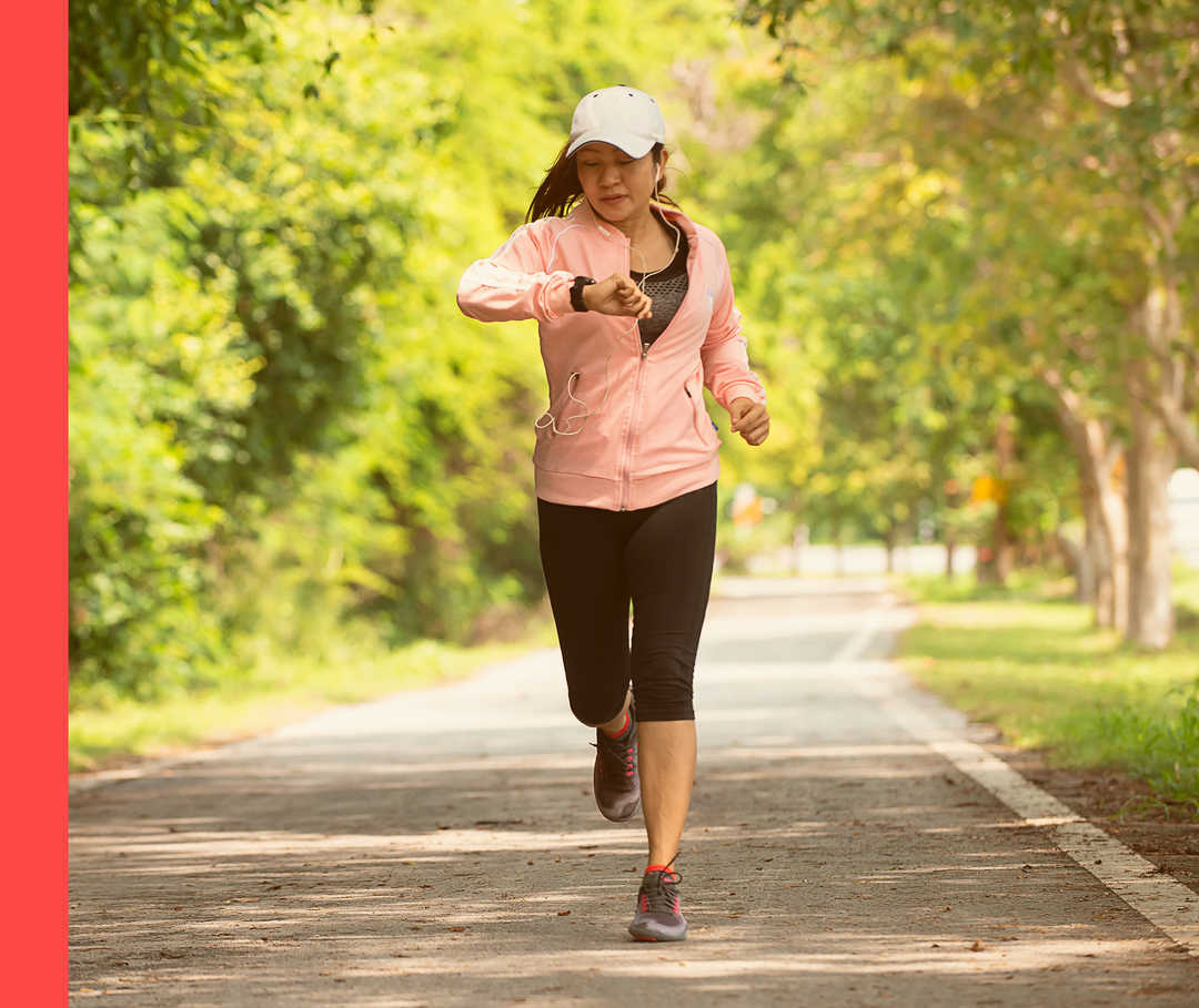 Person in Sportbekleidung joggt im Freien und schaut auf die Uhr an ihrem Handgelenk.