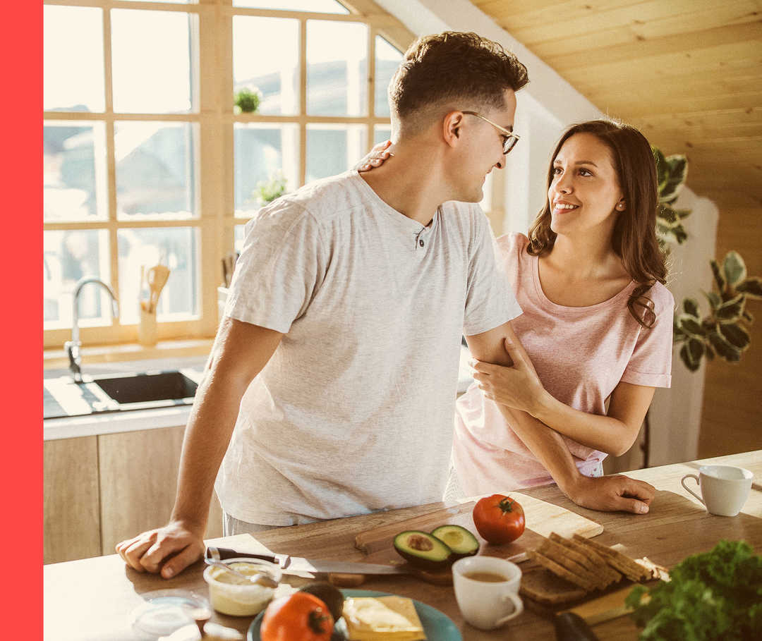 Ein Mann und eine Frau stehen an einer Küchenarbeitsfläche mit Lebensmitteln und schauen sich an.
