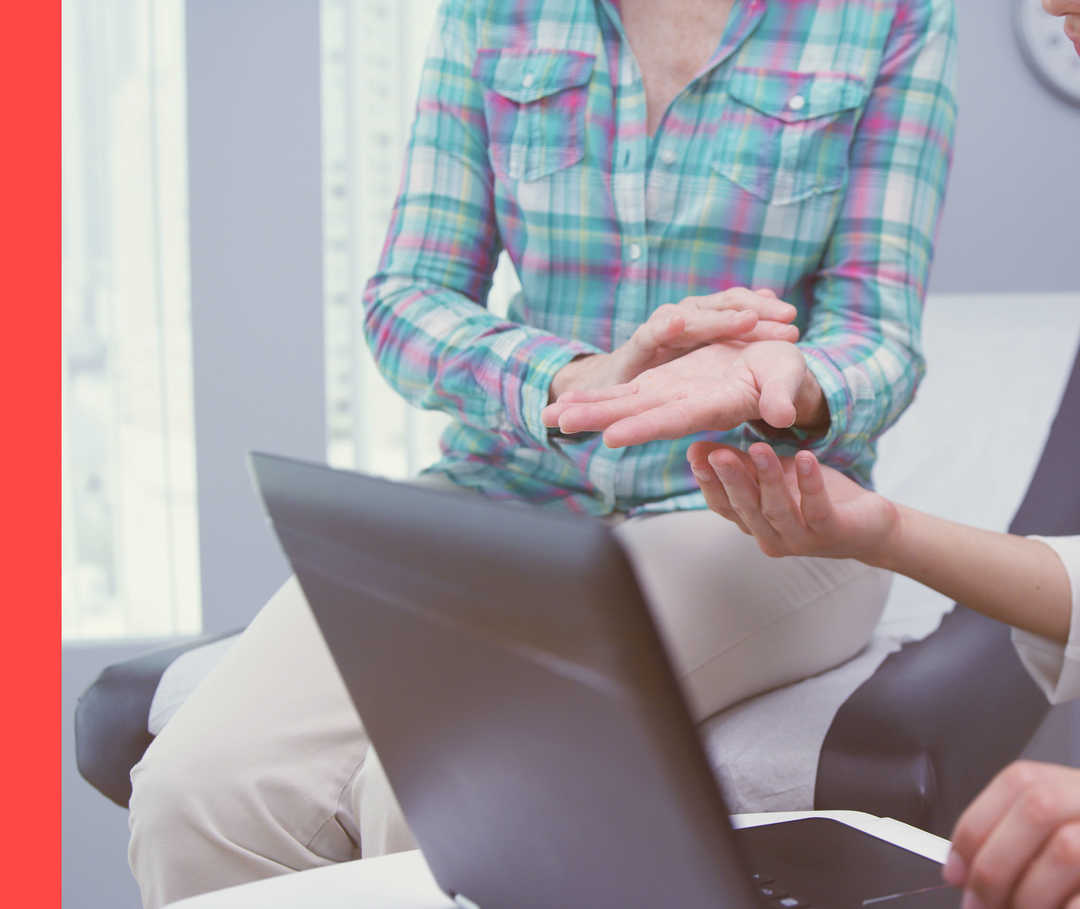 Ärztin mit Laptop und Stethoskop spricht mit Patientin, die ihr ihre Hand zeigt.