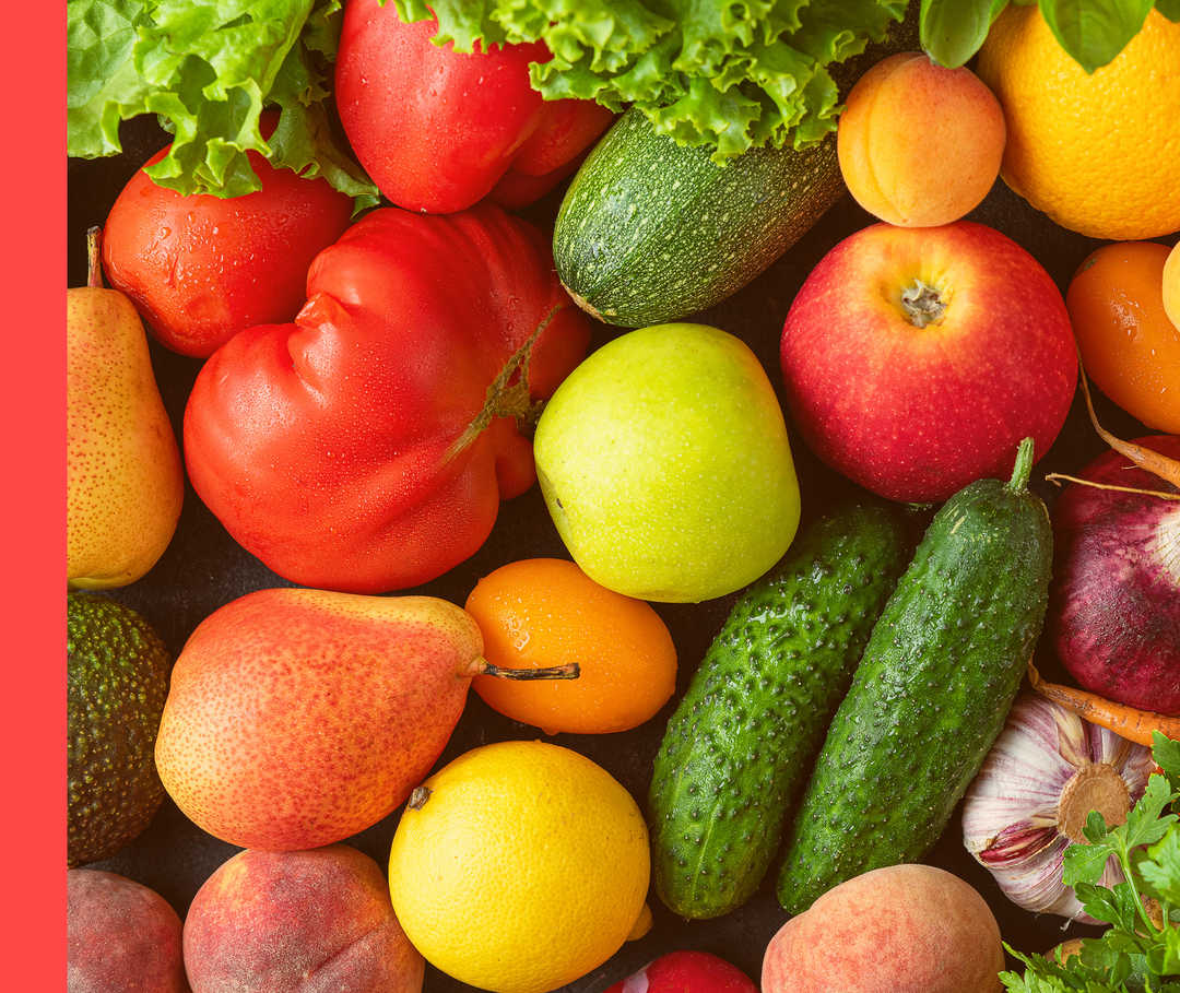 Buntes Obst und Gemüse wie Gurken, Möhren und Äpfel liegt durcheinander.