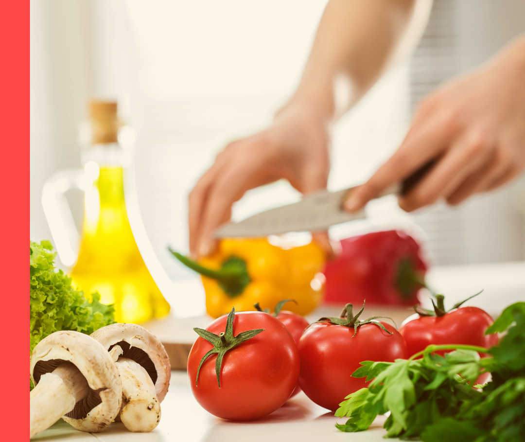 Auf einem Tisch mit verschiedenen Gemüsesorten wird eine gelbe Paprika geschnitten.