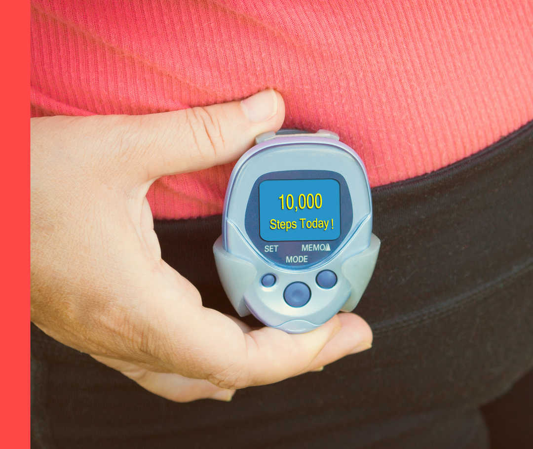 Hand hält Stoppuhr vor Hüfte und Bauch in Trainingskleidung mit Aufschrift „10.000 Steps Today!“ auf dem Display.