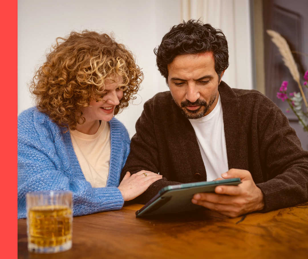 Ein Mann und eine Frau sitzen an einem Tisch und schauen auf einen Tablet-PC.