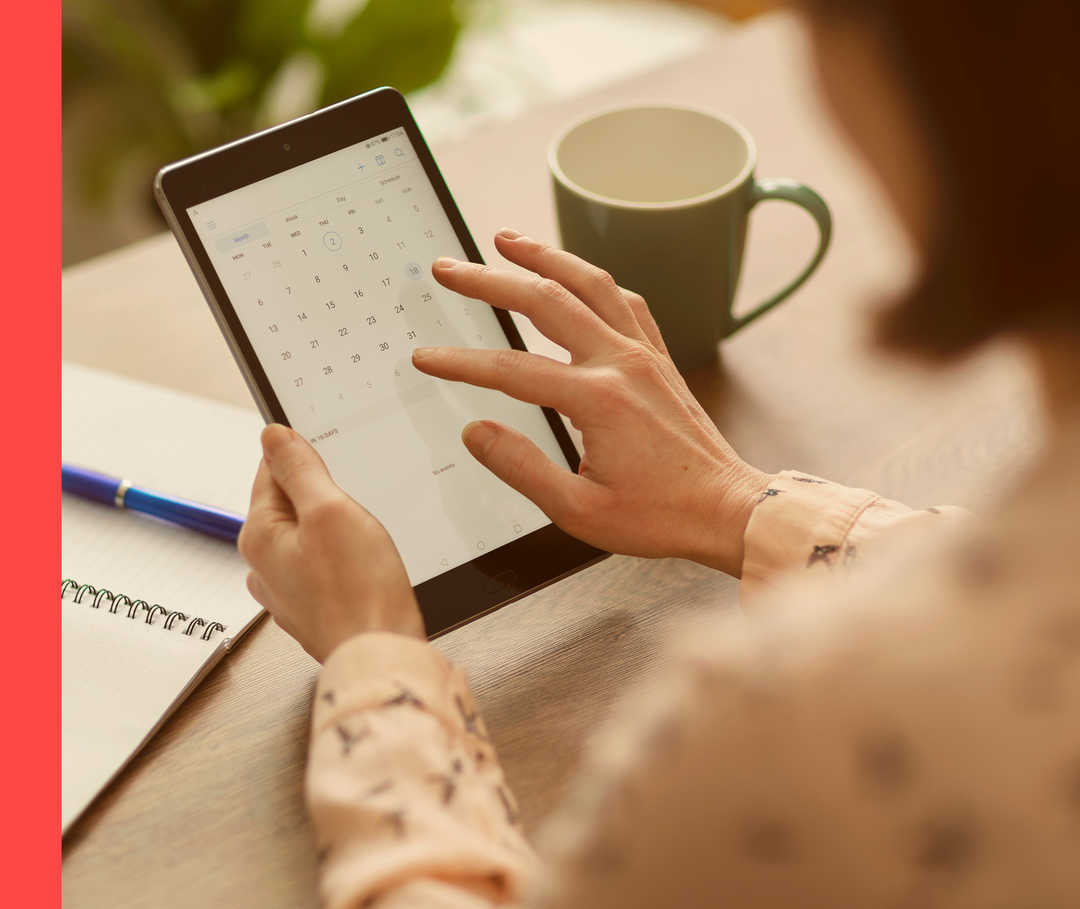 Nahaufnahme von zwei Händen, die ein Tablet mit einem Kalenderblatt halten.