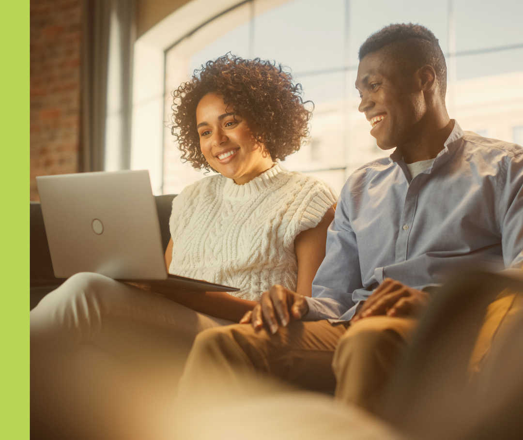 Eine Frau und ein Mann sitzen auf einem Sofa und schauen auf einen Laptop.