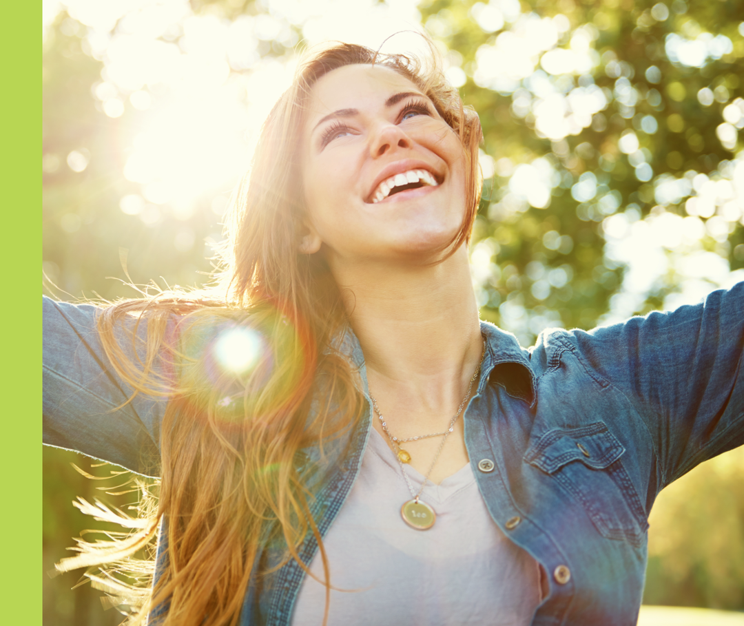 Eine Frau lächelt und breitet im Freien ihre Arme aus.