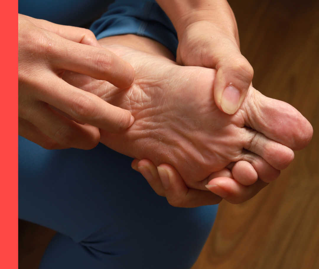 Eine Person kratzt sich mit der rechten Hand an der linken Fußsohle.