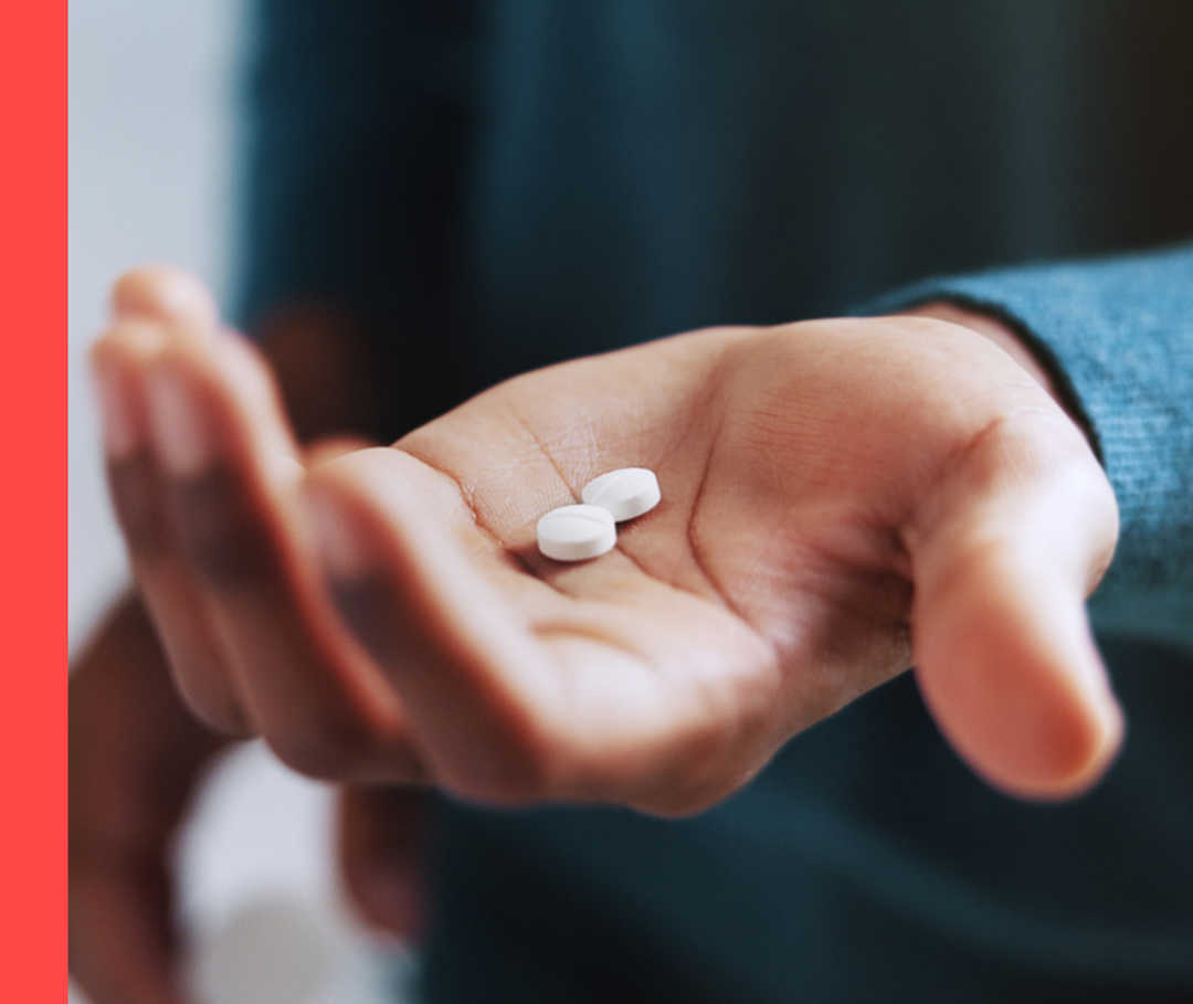 Eine Person hält in der linken Handfläche zwei weiße Tabletten.