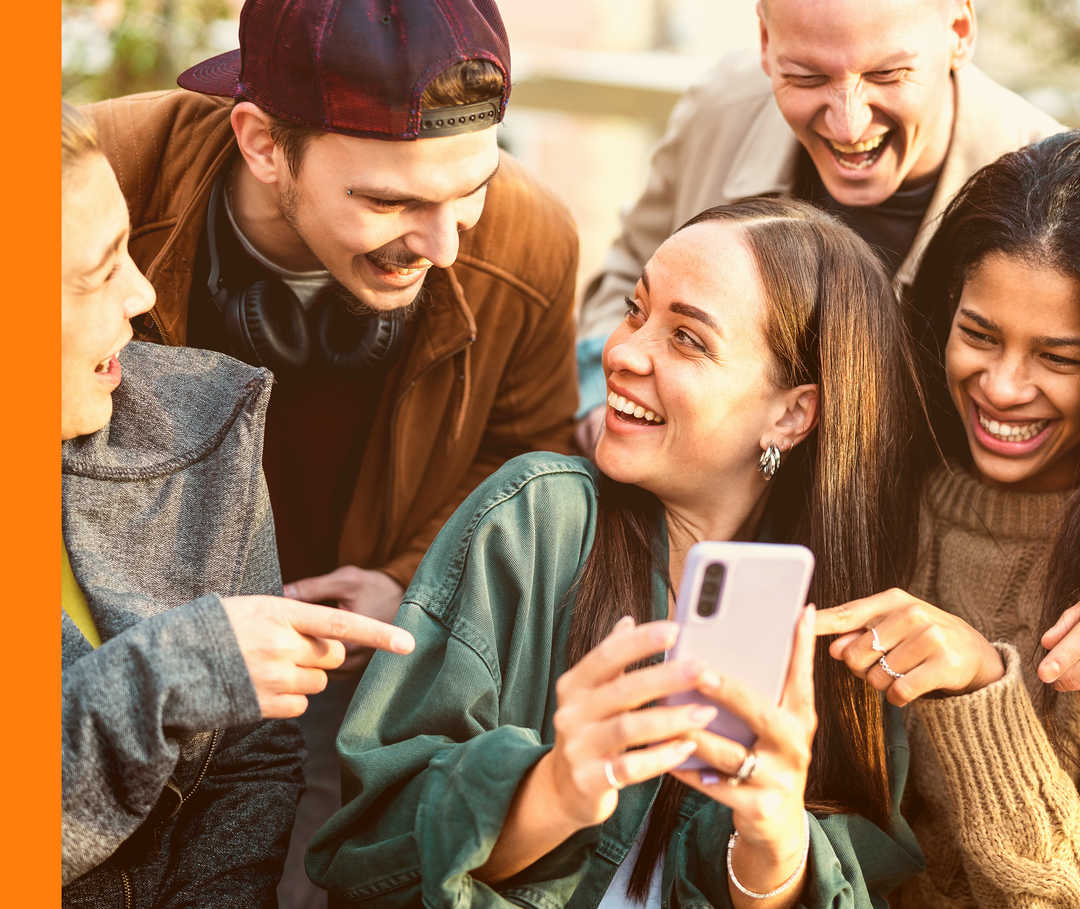Mehrere Personen lachen gemeinsam und zeigen auf ein Smartphone.